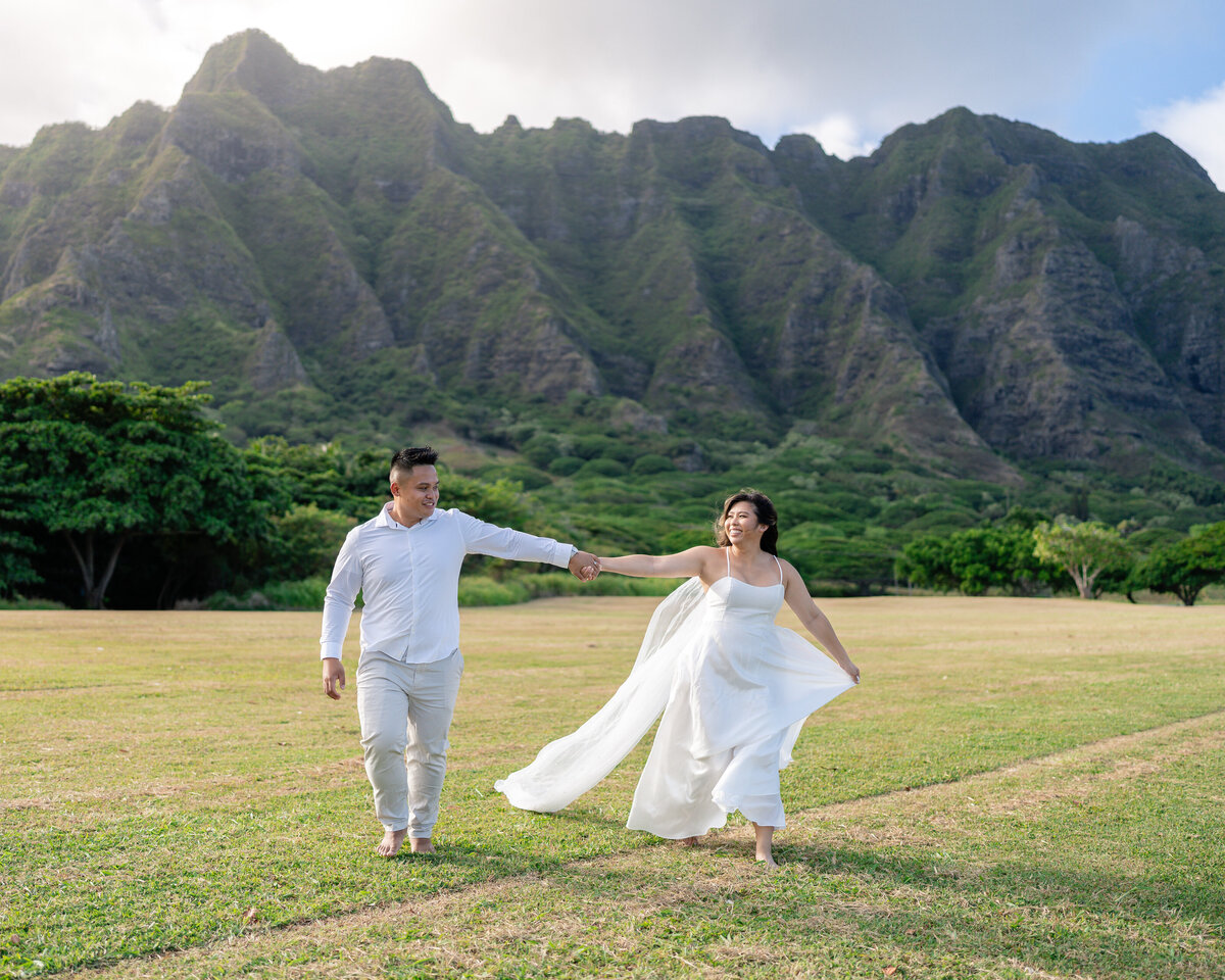Oahu Hawaii Elopement Asian couple holding hands at Kualoa Regional Park during sunset with mountains.