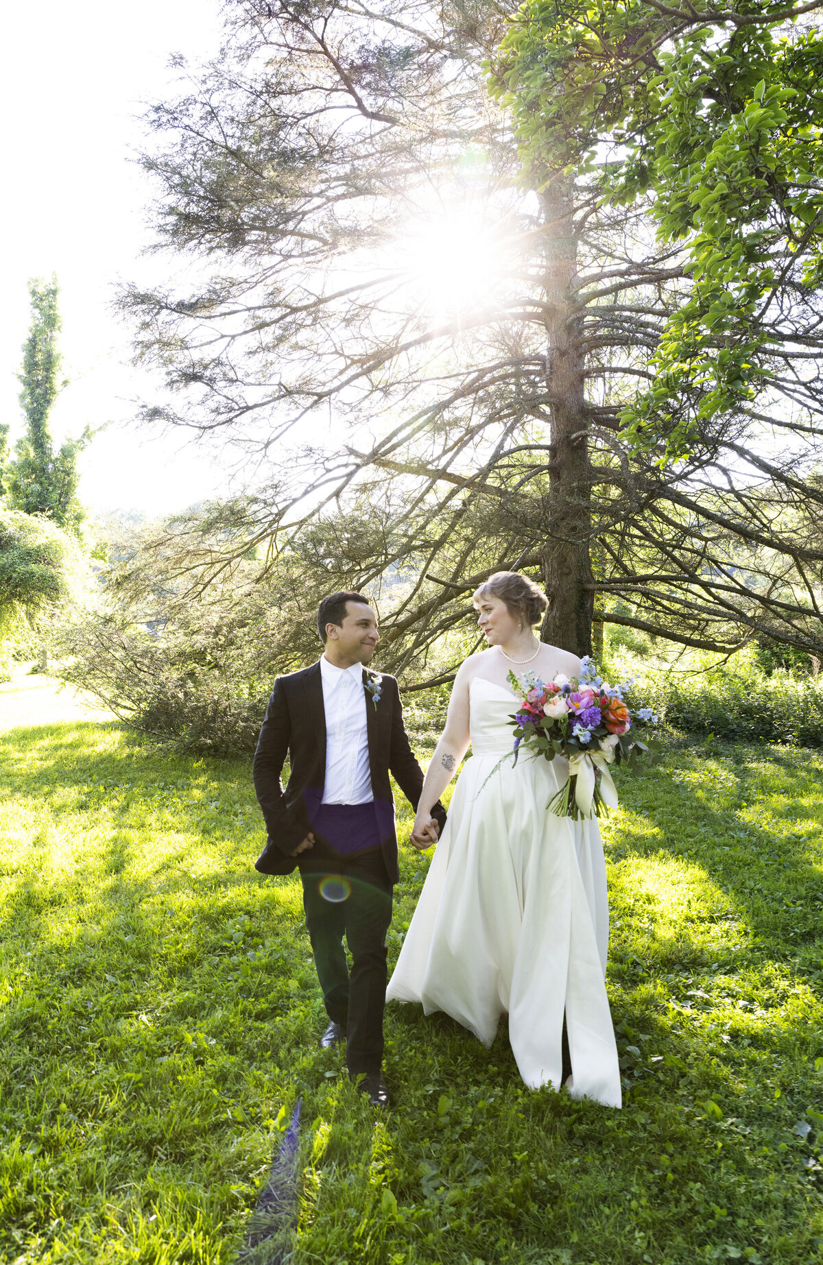 Groom and bride holding wedding bouquet walking through the Tyler Arboretum in Pennsylvania after just getting married