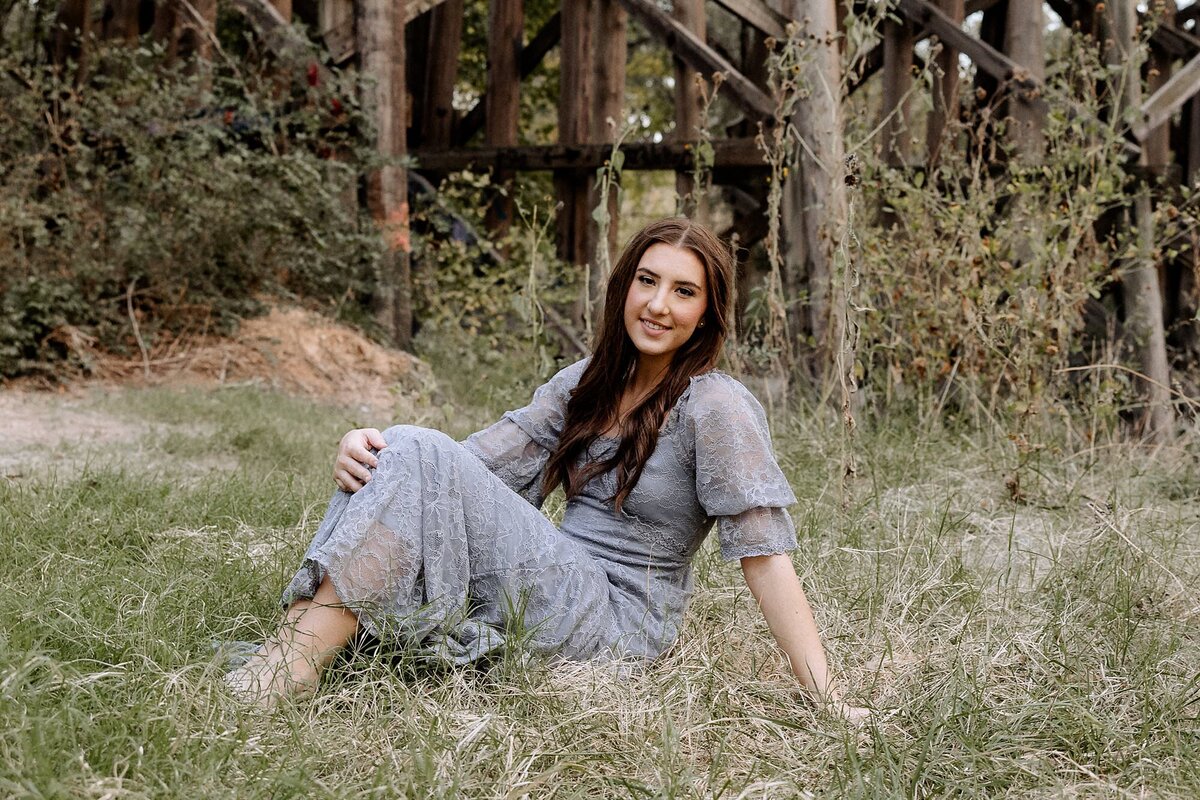 Lubbock senior sitting in a field of green grass. She is wearing a  blue dress.