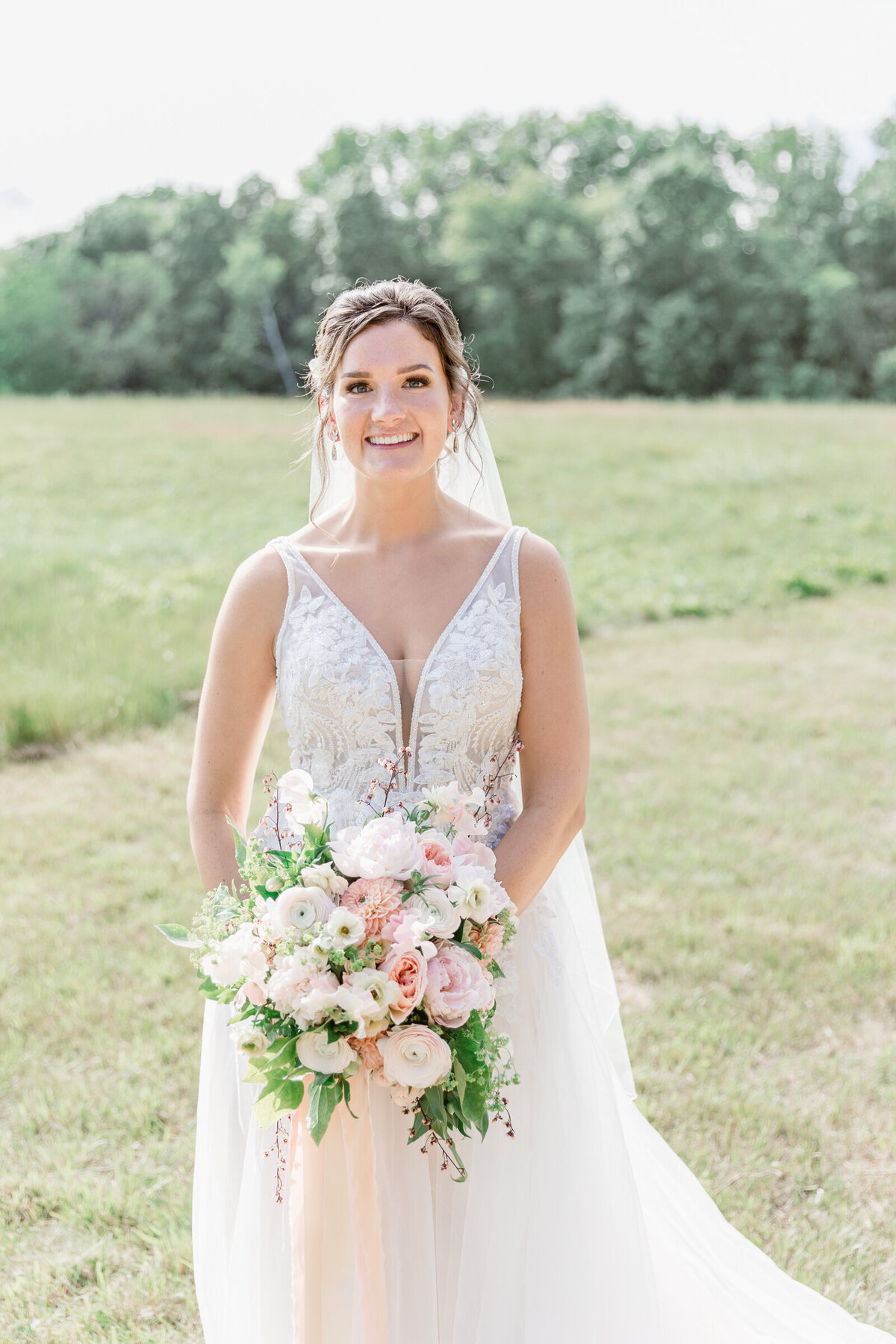 A bride in a soft romantic dress with a large garden style bouquet with pink hues