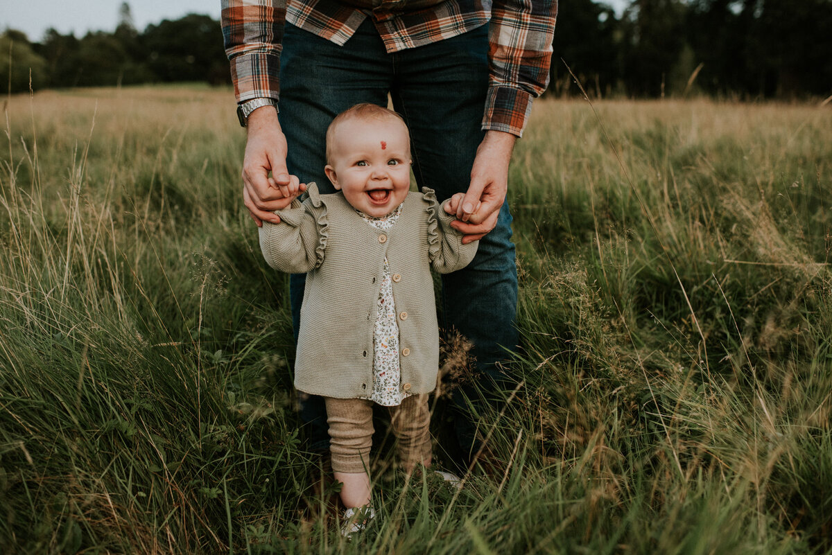 happy baby holding hands with parent in tall grass
