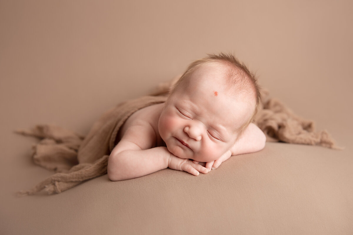 Baby on a beige background sleeping on his stomach and leaning forward on his hands.