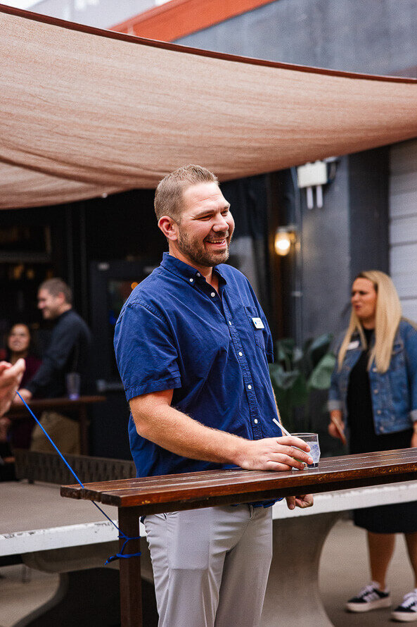 Man holds onto drink and laughs while watching a group of people.