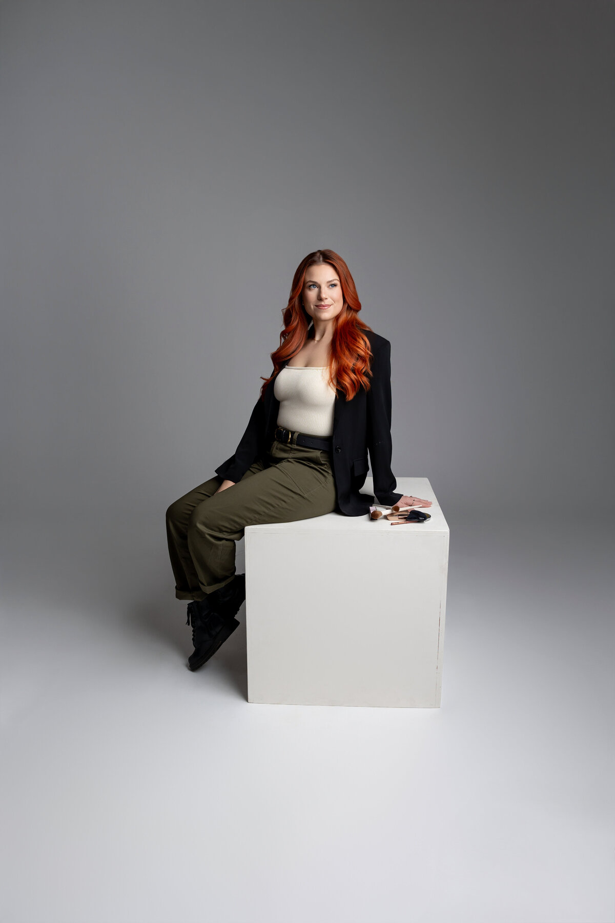 Red-haired woman seated on white cube posing with hand in hair. Photograph by Yucaipa branding photographer Kaitlyn Dawn Photography.