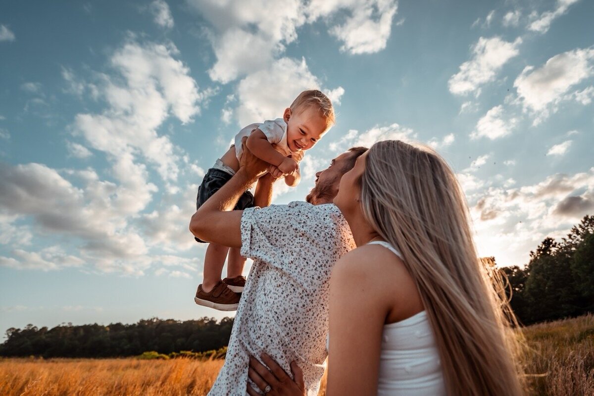 Mother and Father play with their child at sunset in an open field