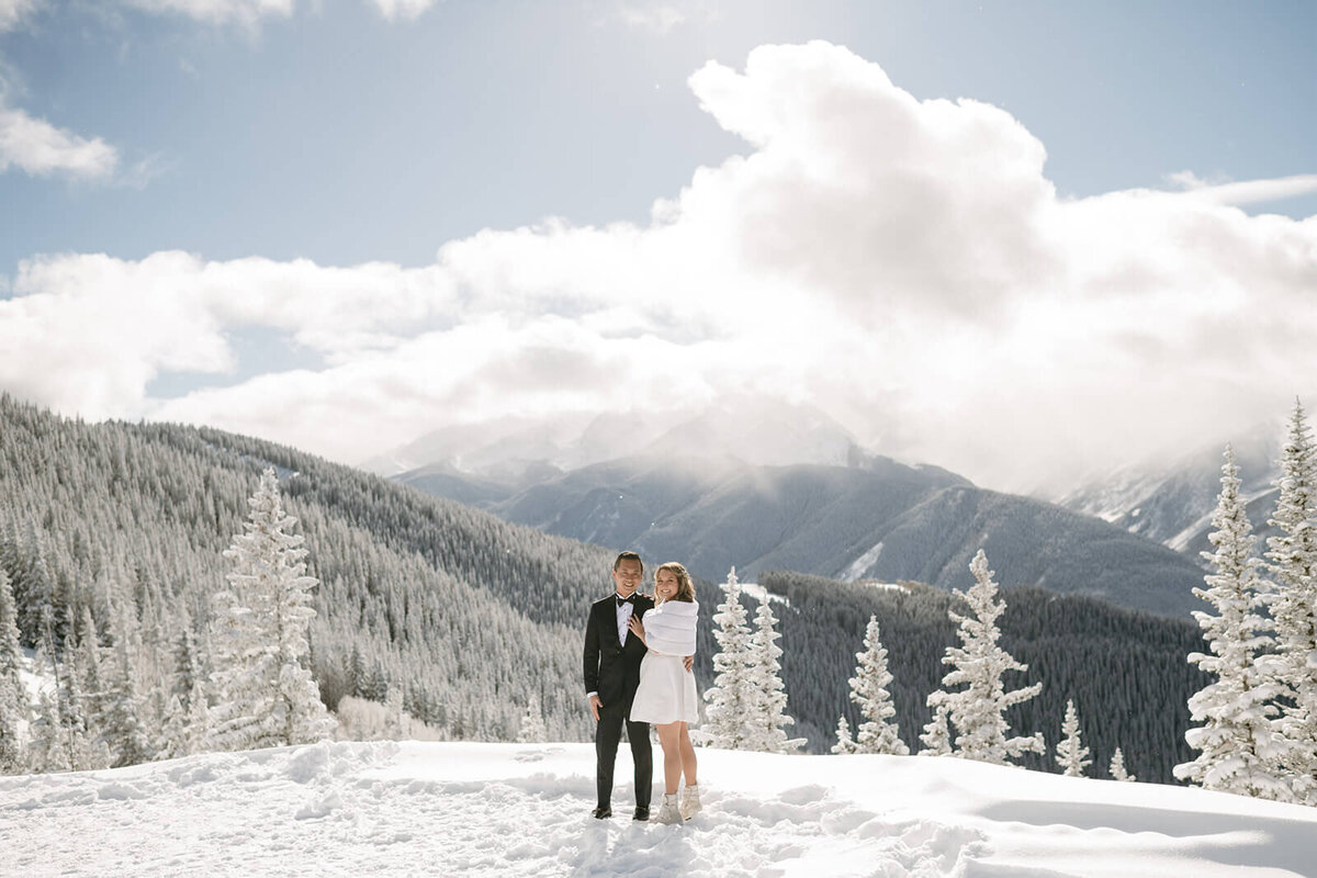 Bride and groom on a mountaintop at St. Regis Aspen, surrounded by sweeping views of snow-capped peaks and blue skies.