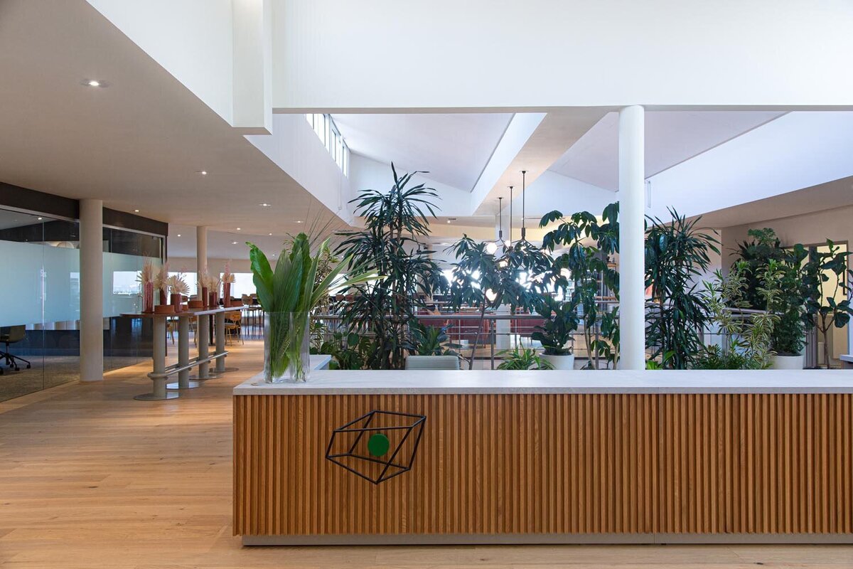 Reception desk with wood slat front, greenery, and an open upper-level workspace behind it.