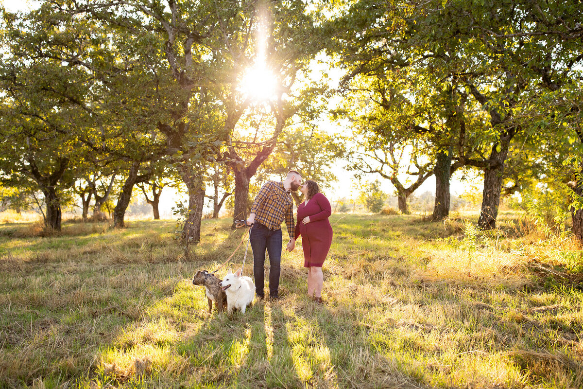 Expecting couple with two dogs holding hands in a park in Portland area. The sunsets behind them on a fall evening. 
