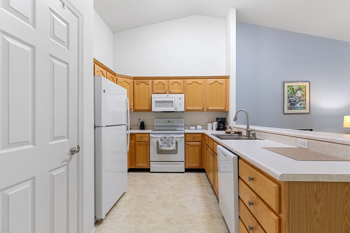 Interior photo of a kitchen inside a home, with light colored wooden cabinets, light colored countertops, and white appliances.