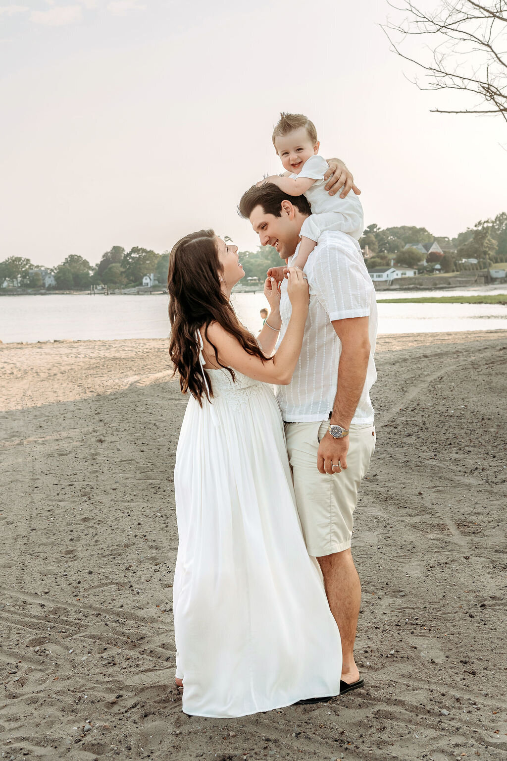 Connecticut maternity photographer captures joyful family moment with toddler on father's shoulders at beach