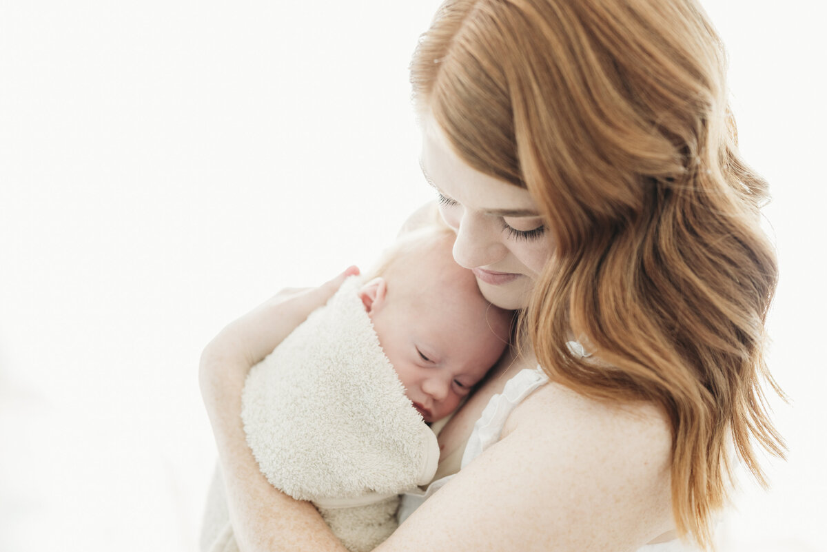 Mother holding her swaddled baby close with soft natural light during an intimate Kansas City newborn photography session.