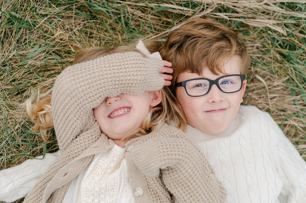 Siblings laying in the grass, smiling up at the sky