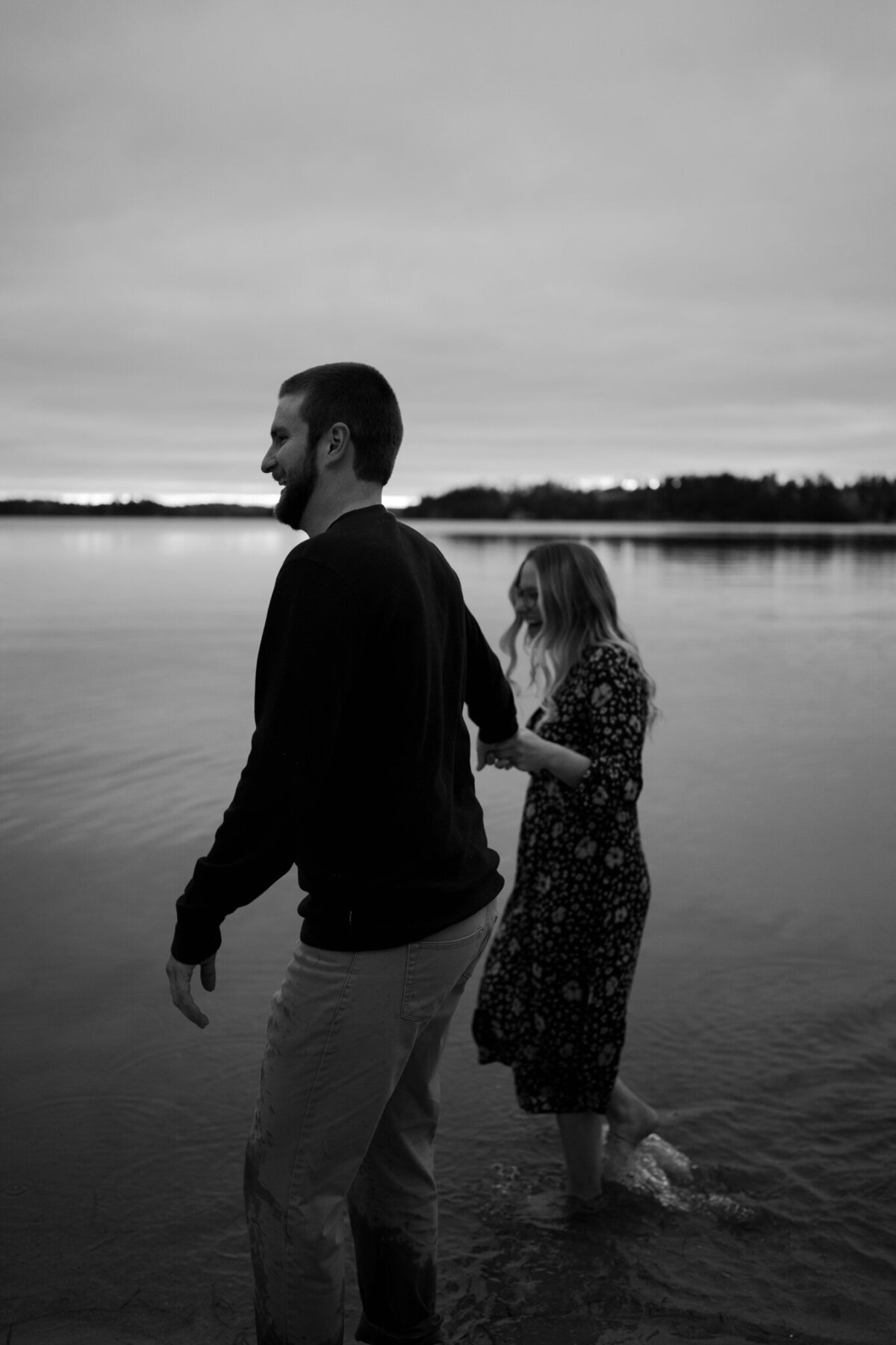black and white image couple holding hands walking in lake