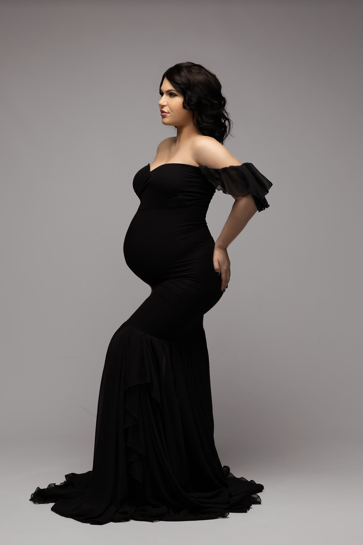 Dallas maternity photography featuring woman in sleek black gown with stylish off-the-shoulder design.