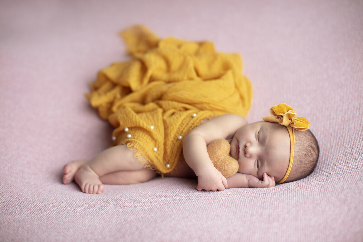 Newborn girl layign on pink snuggling yellow heart