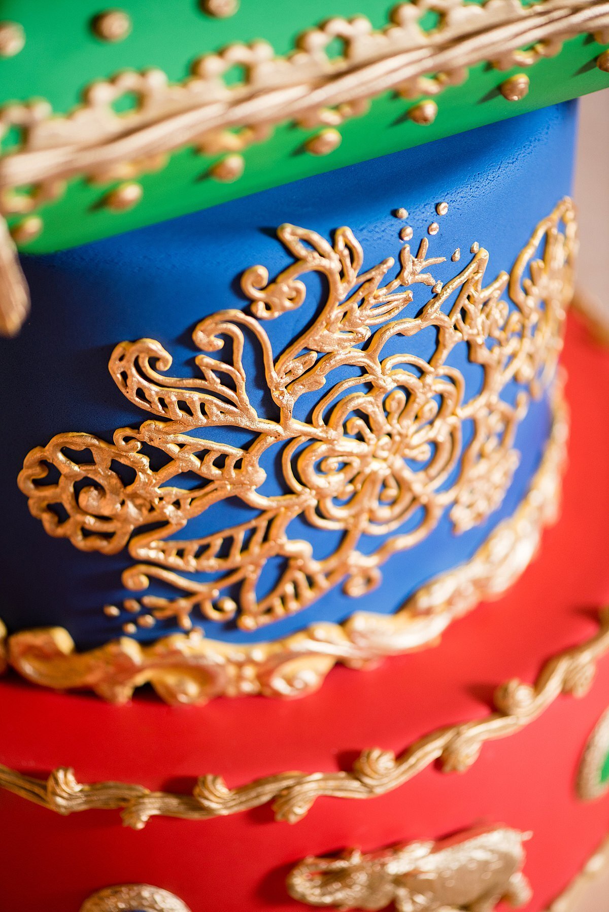 Close up image of a red, blue and green wedding cake for a Hindu wedding with gold elephants and gold mandala detail
