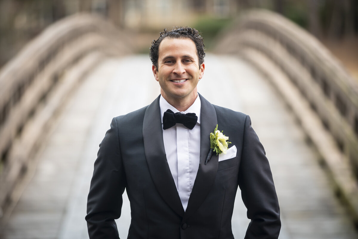 Groom standing in front of a wooden bridge.