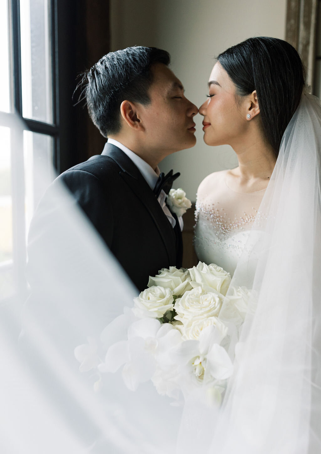 Groom leans in to kiss bride in her veil inside of the Sweeney Barn in Manassas