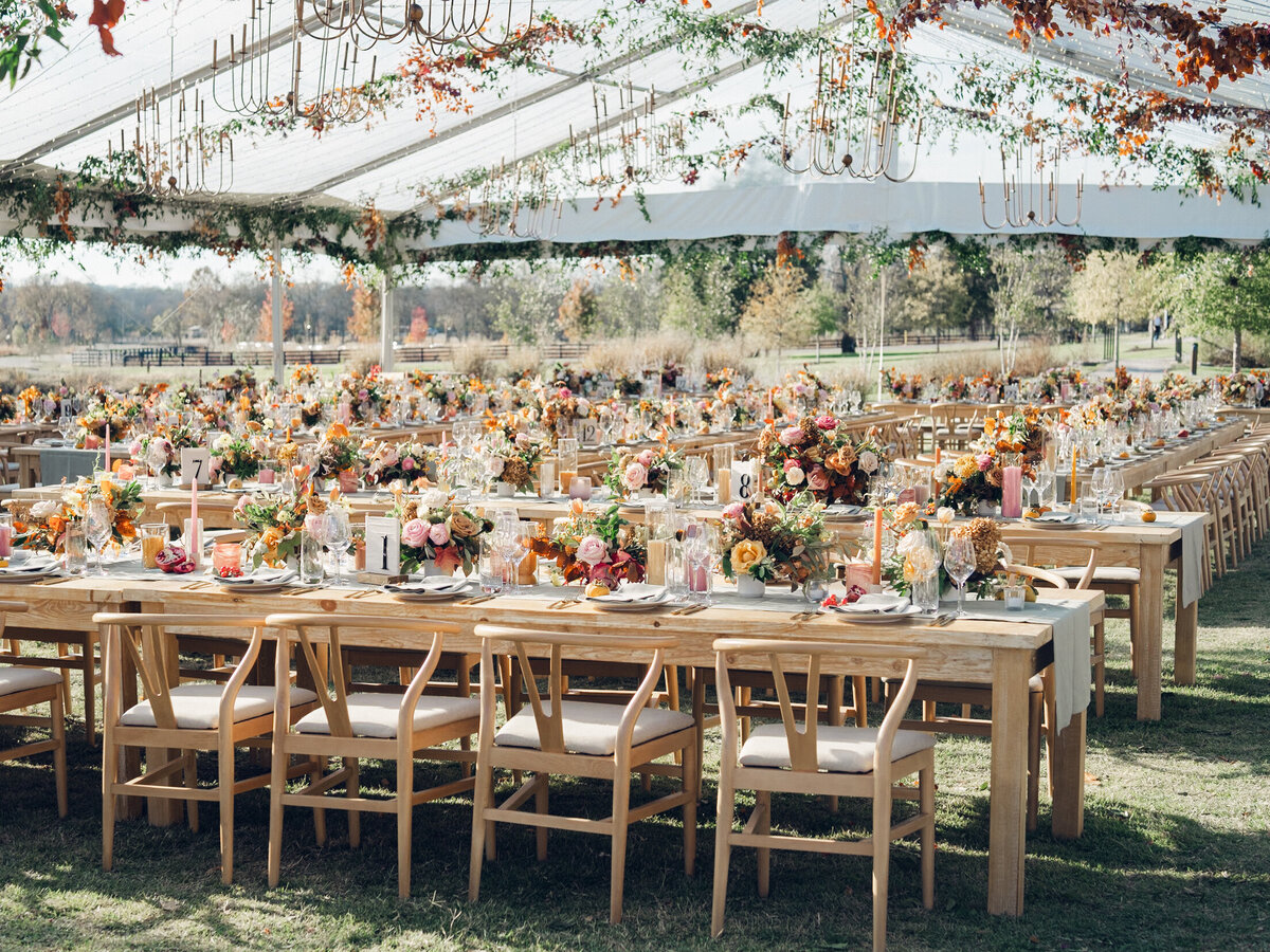 Full tablescapes of fall flowers create lush warm fall setting for wedding reception in Tennessee countryside. Wedding colors in blush, tangerine, mustard yellow, caramel, and honey. Wedding fall florals consisting of roses, clematis, ranunculus, brown tulips, and fall foliage. A collection of low centerpieces and accent arrangements create lush floral wedding reception tables with styled fruit place settings. Unique and colorful candles for reception tables in pink, orange, yellow, and gold. Destination floral design by Rosemary & Finch Floral Design in Nashville, TN.