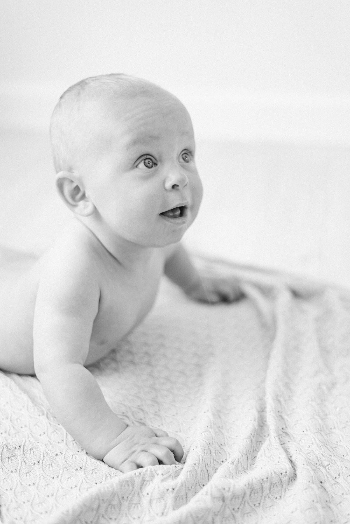 baby boy laying down lifting his head up off blanket at a milestone photography session in Billingshurst