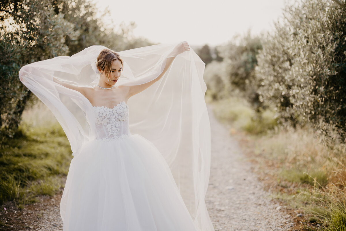 Bride lifting long veil among olive trees at Castello il Palagio Chianti, wedding photographer Tuscany.