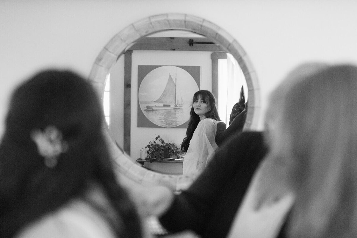 Bride looking in mirror as she has her dress fixed