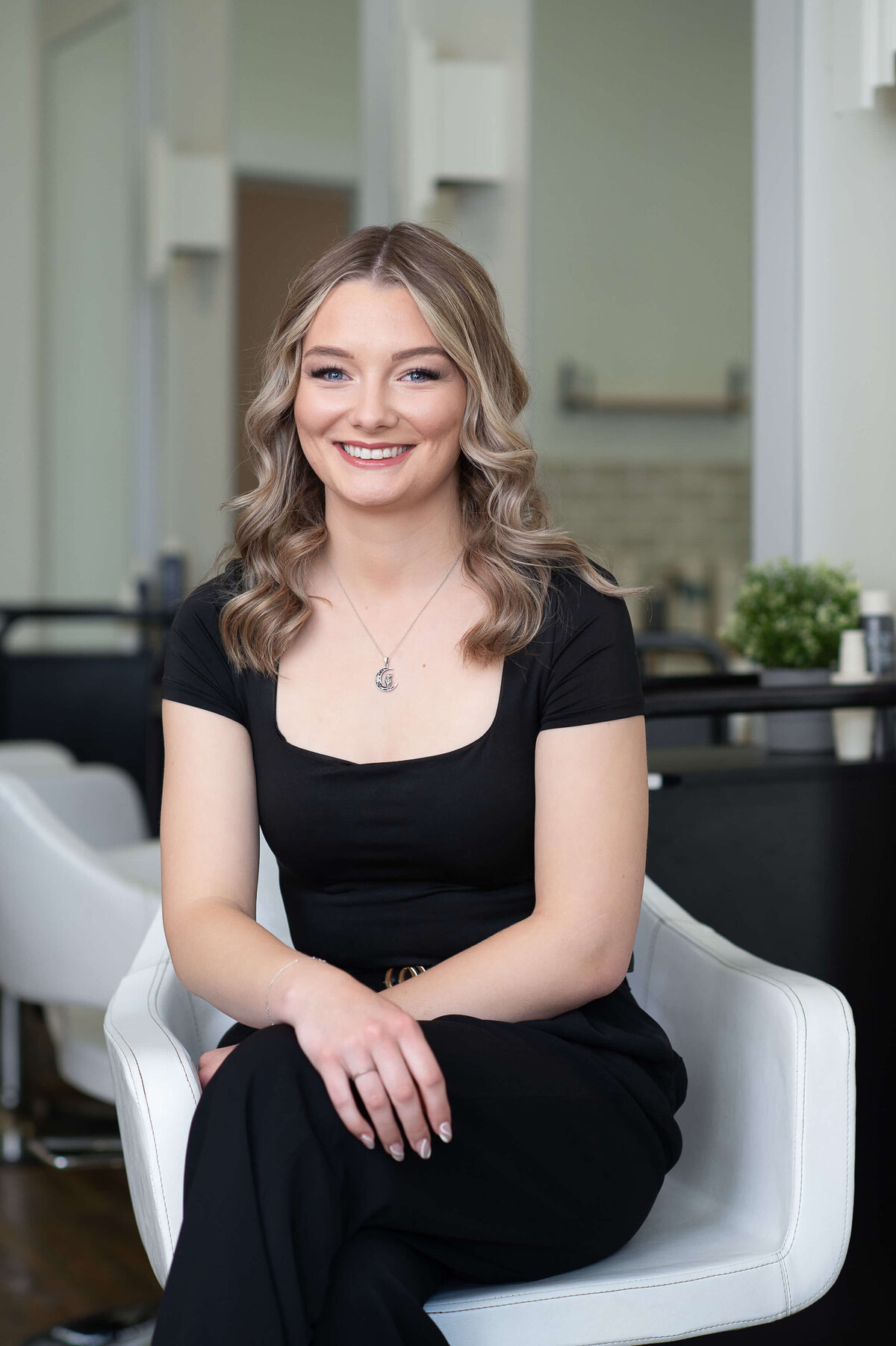 a young hair stylist with long curled hair and dress in black.  Captured on location at Richardson Hair Design by Ottawa branding photographer JEMMAN Photography