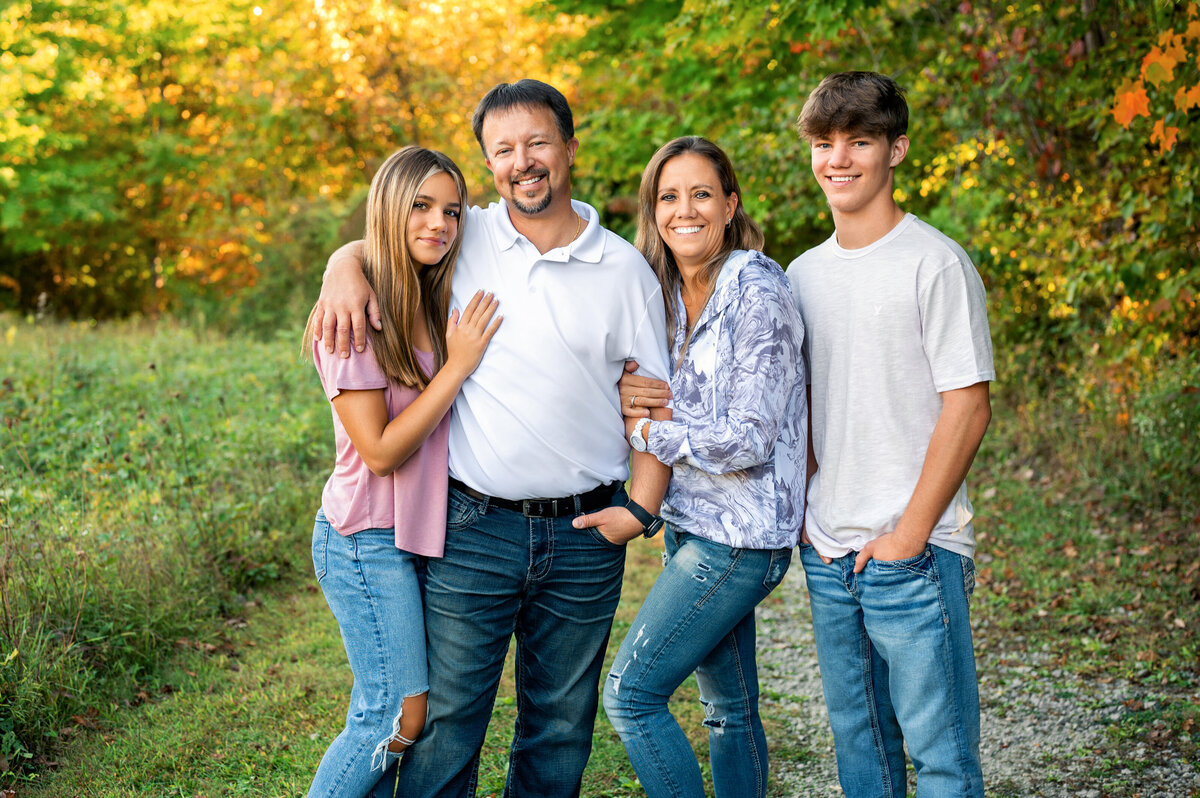 A family of four posing together in a scenic outdoor setting with autumn colors