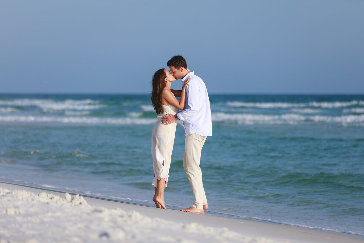 couple posing on water's edge at grayton beach state park after becoming engaged from a surprise proposal.