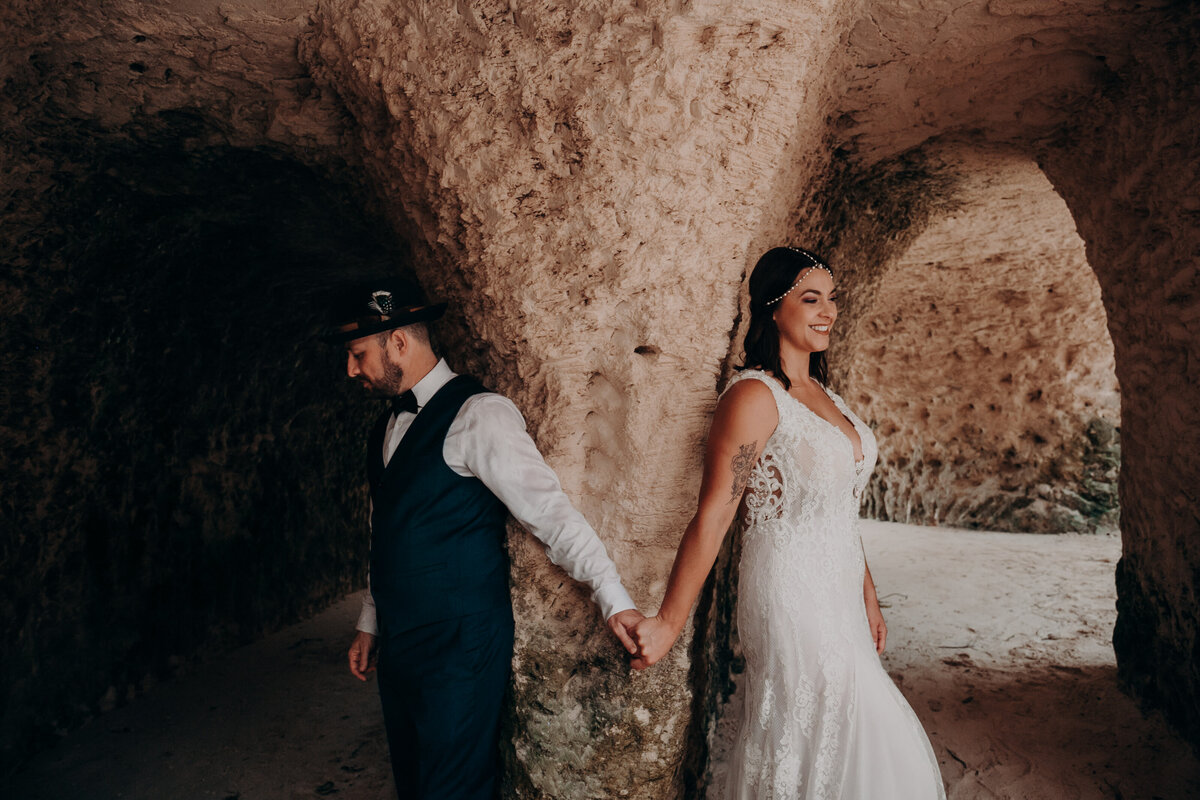 A bride and groom first touch photo in the caves at Xcaret, Mexico by photo + video team The Astralis Collective, Angela Moon Photography. 
