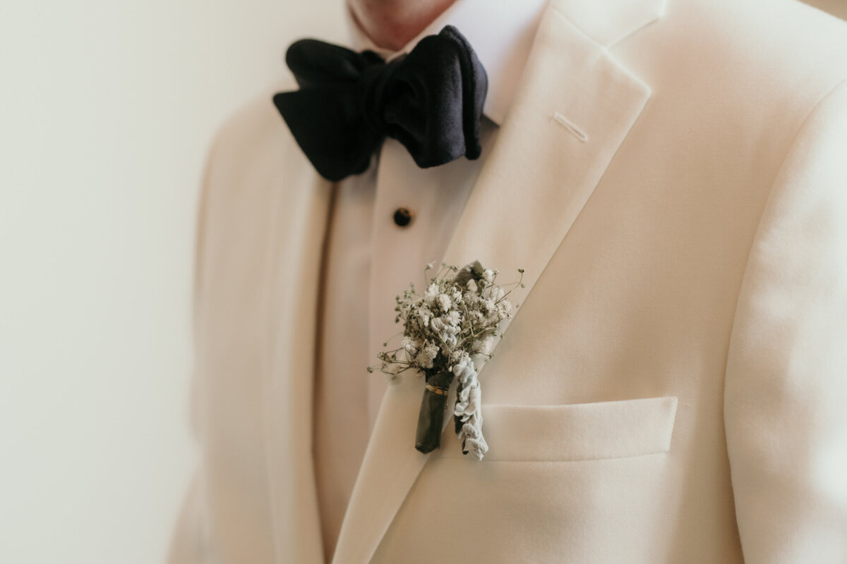Diese Nahaufnahme zeigt den Blumenanstecker aus Schleierkraut, den der Bräutigam am Revers trägt.