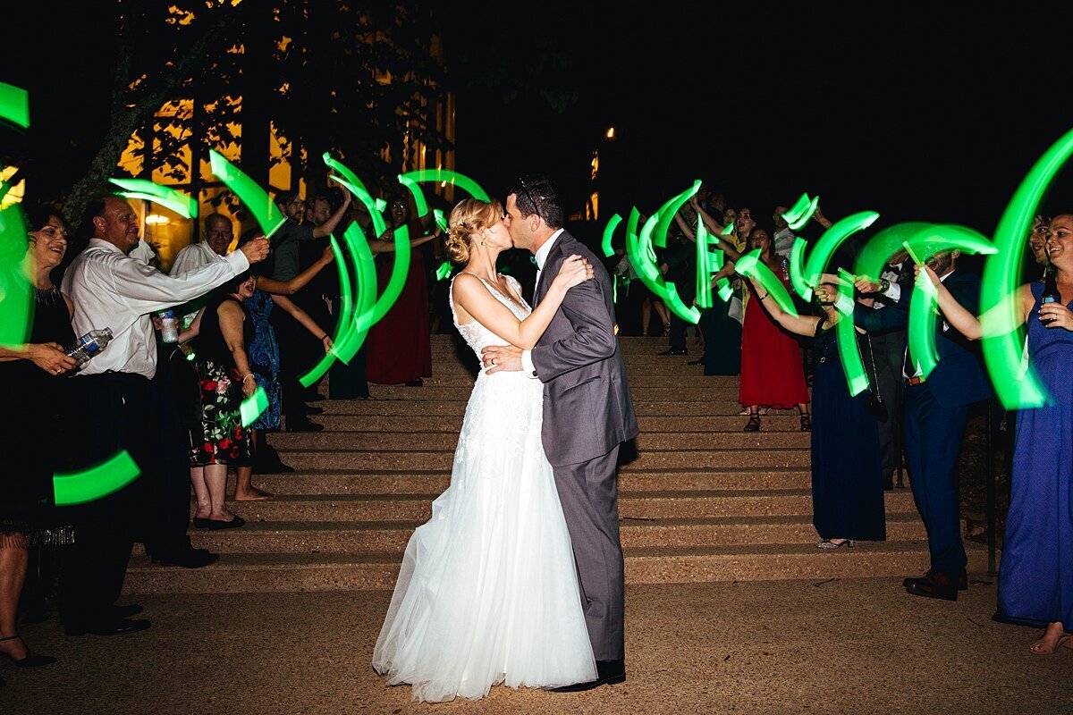The bride and groom kiss at the bottom of the steps at Cheekwood Botanical garden as their guests swing long glow sticks in the air during the wedding send off.