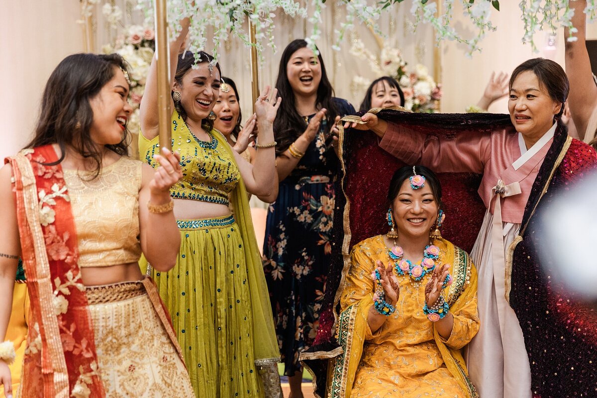 A bride, her family, and her wedding party take part in a traditional Pithi Ceremony on her wedding day in Dallas, Texas. Everyone is wearing traditional, celebratory, cultural garb.