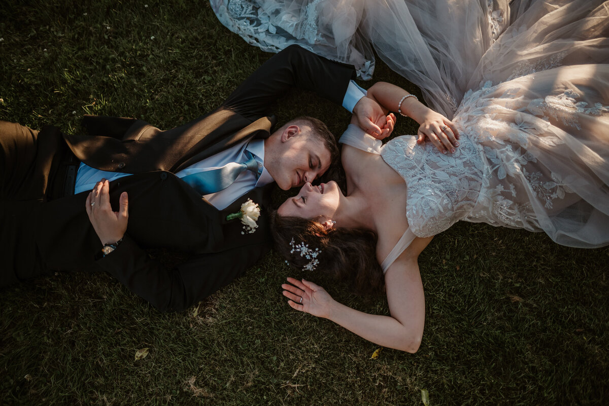 Sunset wedding in Port Gamble, WA. Bride and Groom in wedding attire laying in grassy field.