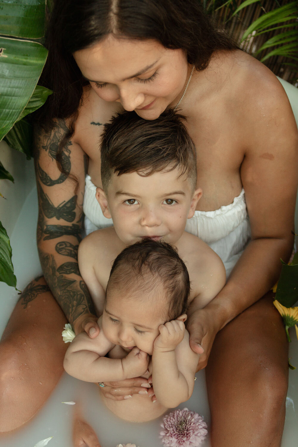 Mother and her two children sharing a moment in the milk bath, older brother embracing the baby