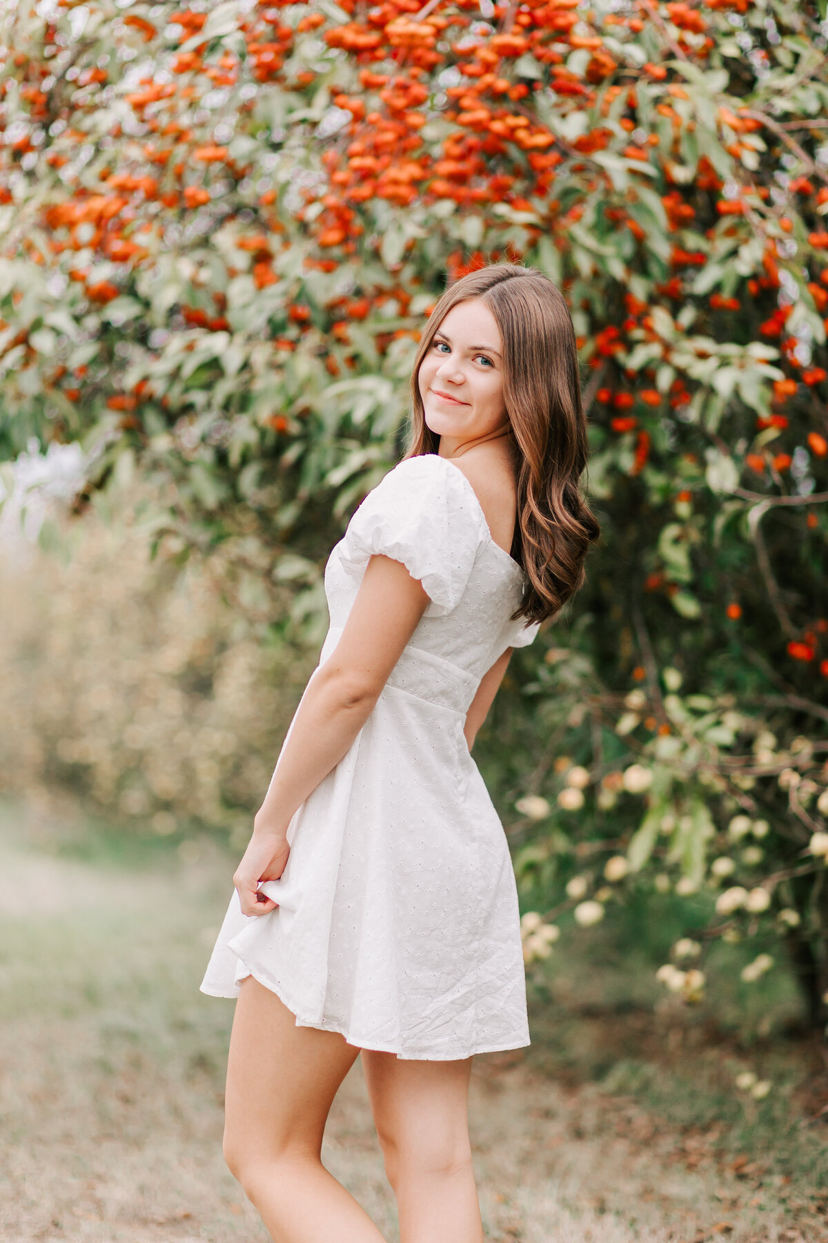 A senior girl in a white dress looks over her shoulder  by a crabapple tree at Adair's Orchards in Albany, OR