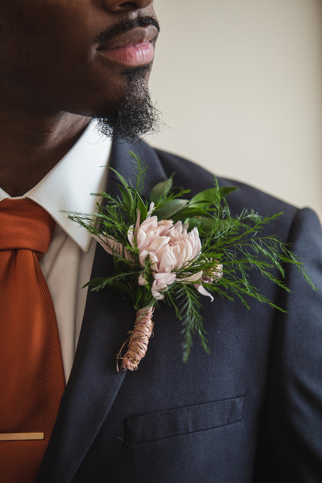 close up of groom in a navy suit with a copper tie and a pink boutonniere