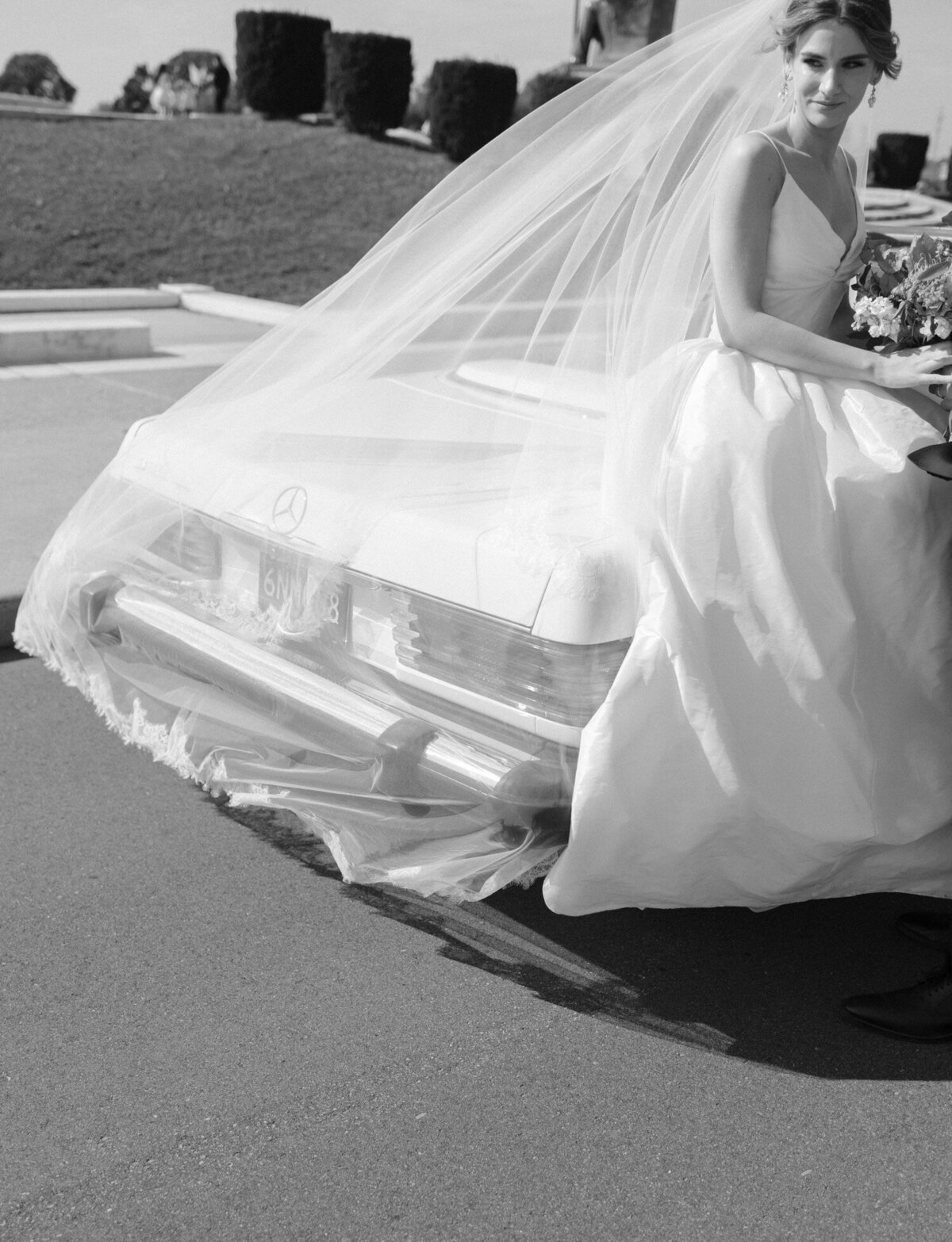 bride sits on vintage convertible with long cathedral veil in Detroit, Michigan