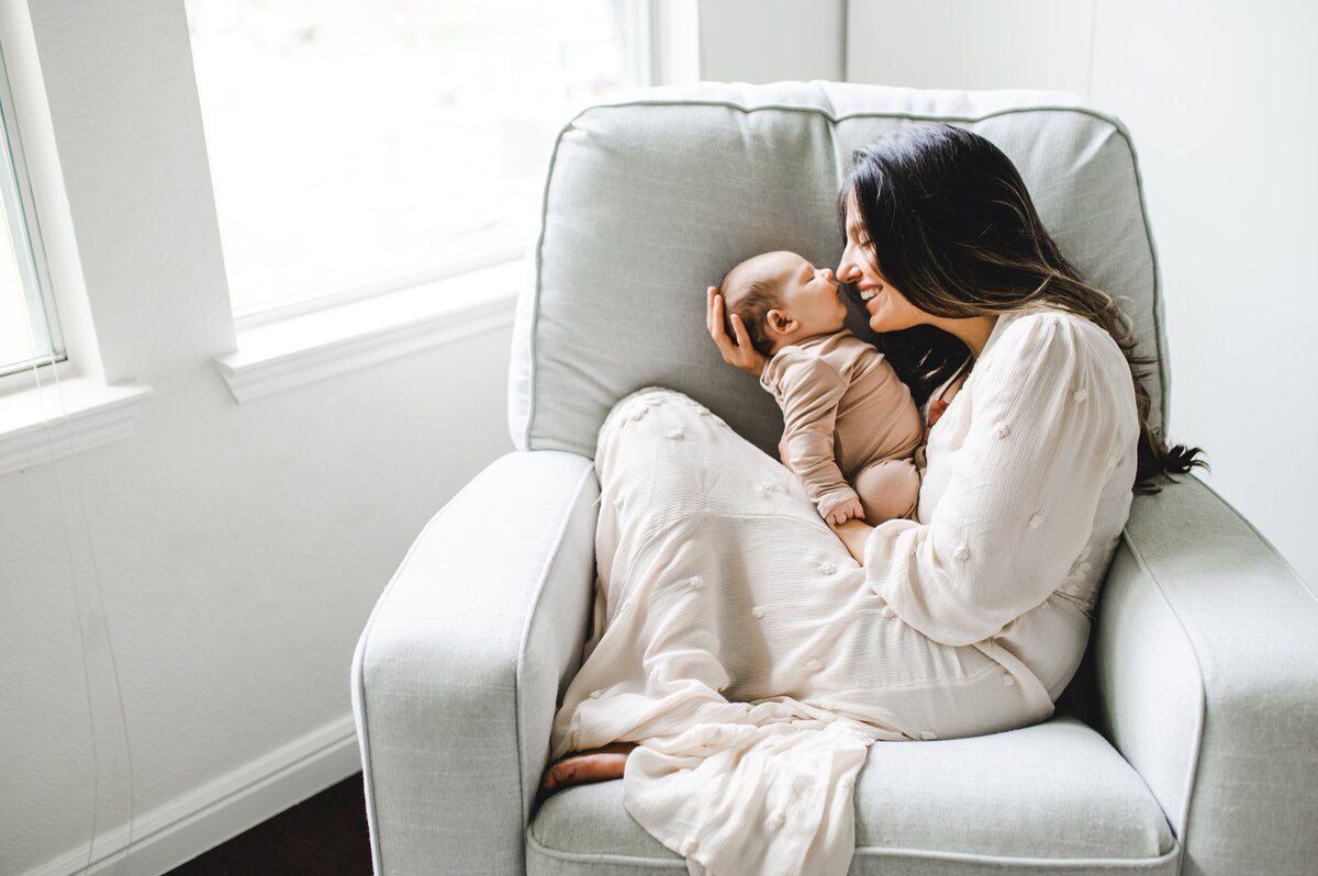 a new mom holds her newborn baby in a chair near the window