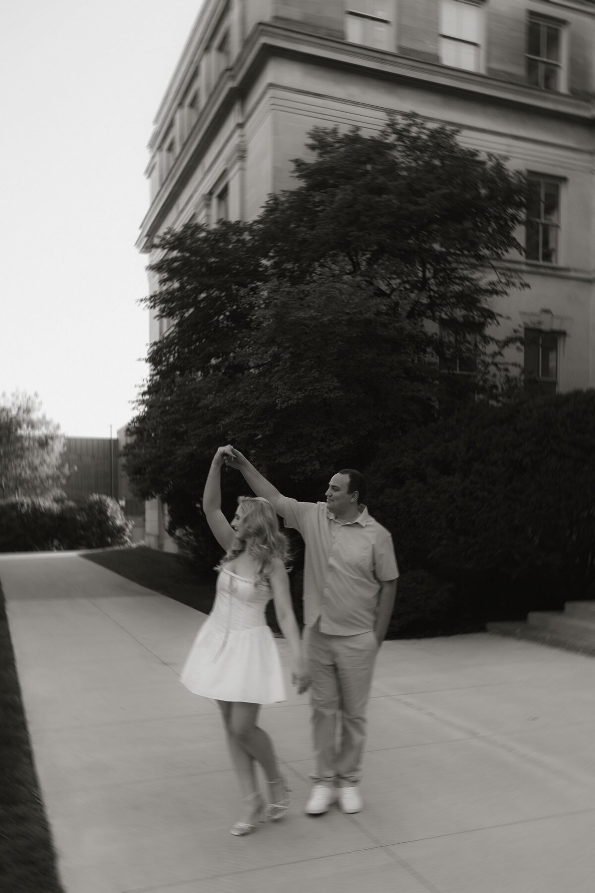 A man twirls his fiancé in her short white dress during their engagement session.