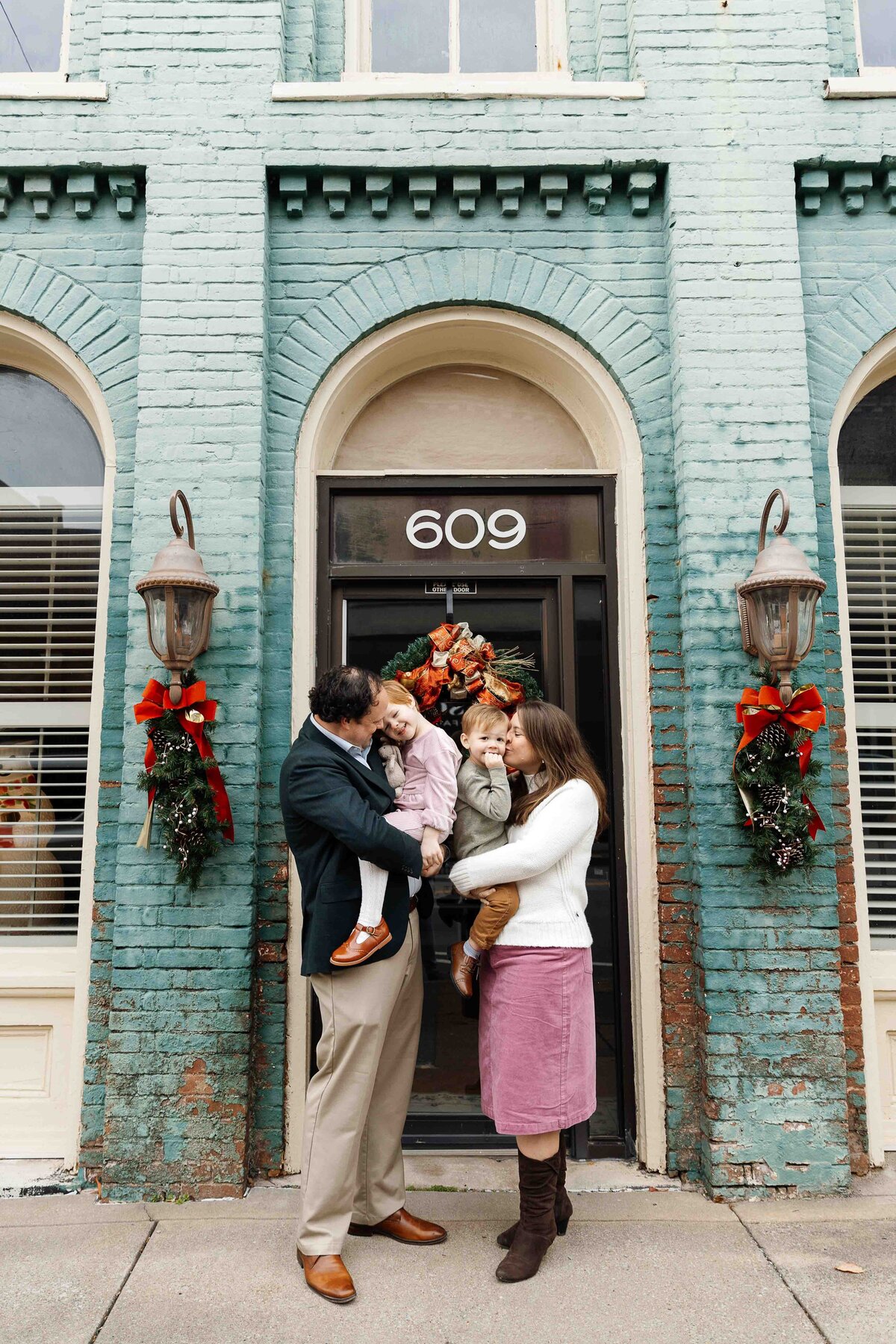 Father holds daughter and mother holds son giving them kisses on their cheeks