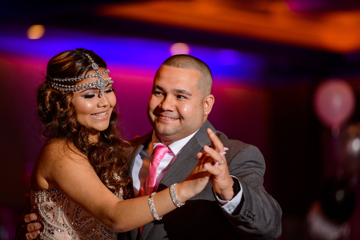 A girl wearing elaborate jewelry dances with a man in a gray suit