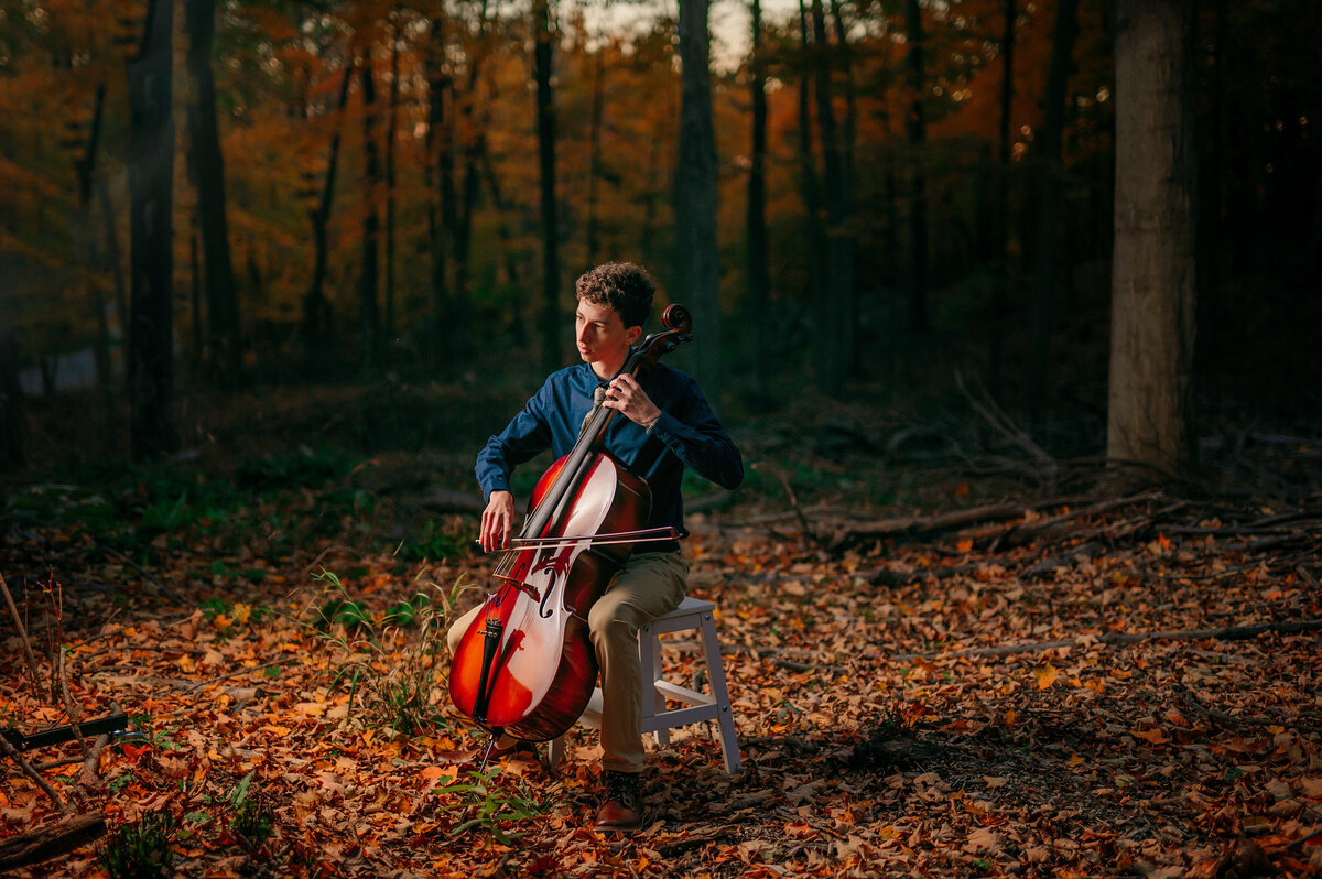 A young man from Waukesha South High School plays his cello surrounded by fallen leaves in Lapham Peak for his senior photos.