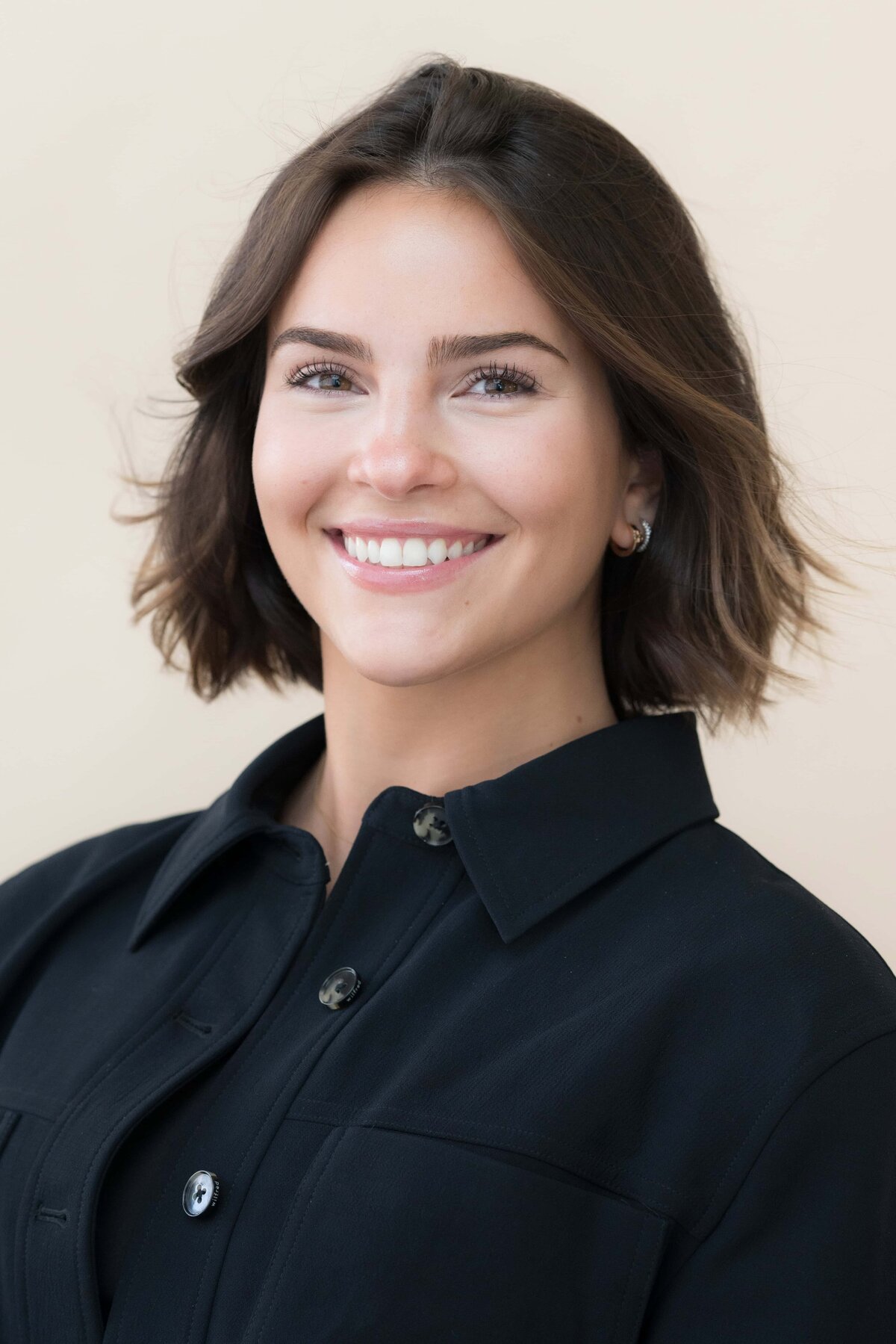 young woman with dark hair smiling while wearing a dark shirt posed for a modeling headshot