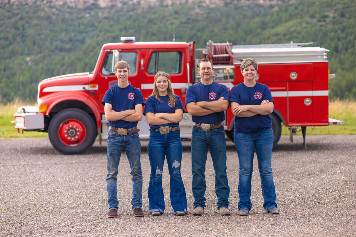 family of four in fire station shirts and jeans posing in front of a fire truck