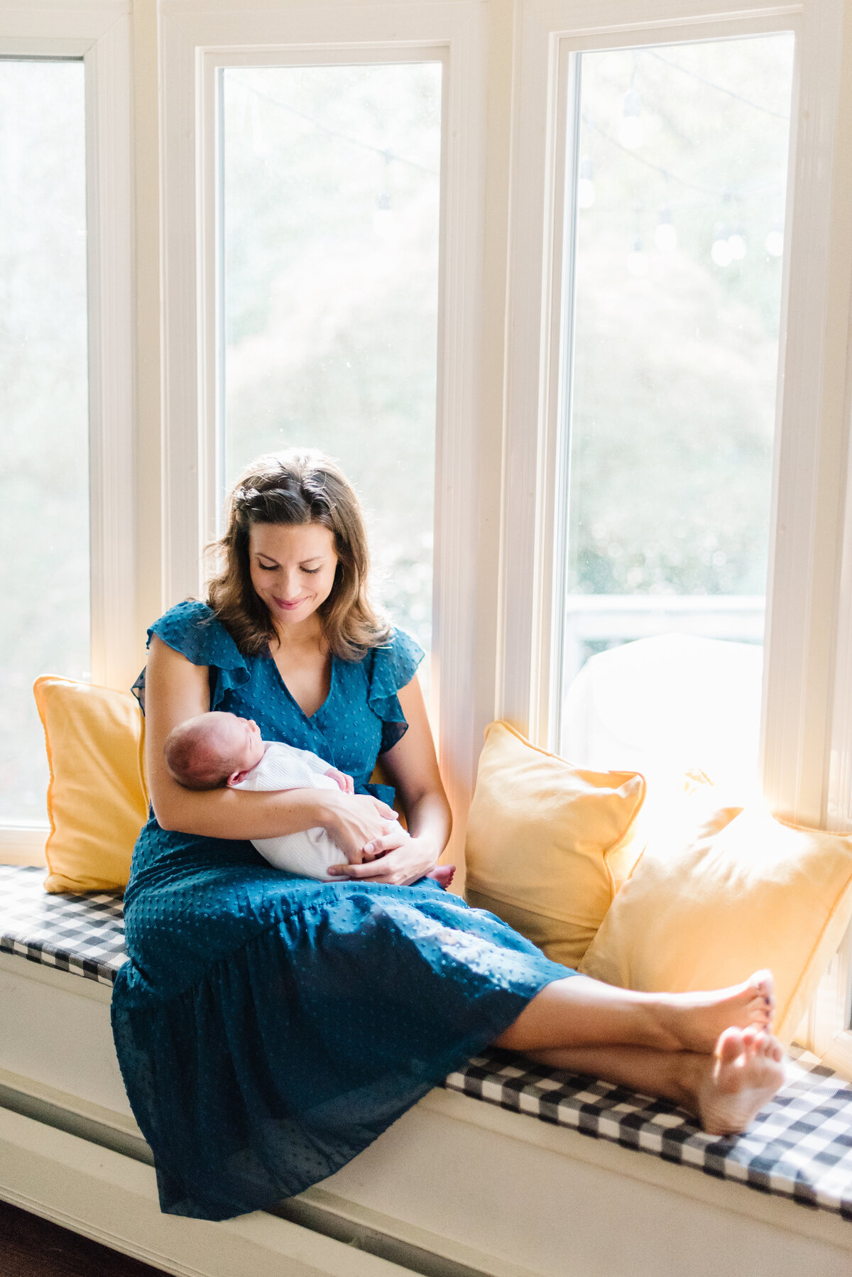 Mom in blue dress sitting on window seat holding newborn - Washington DC Newborn Photographer