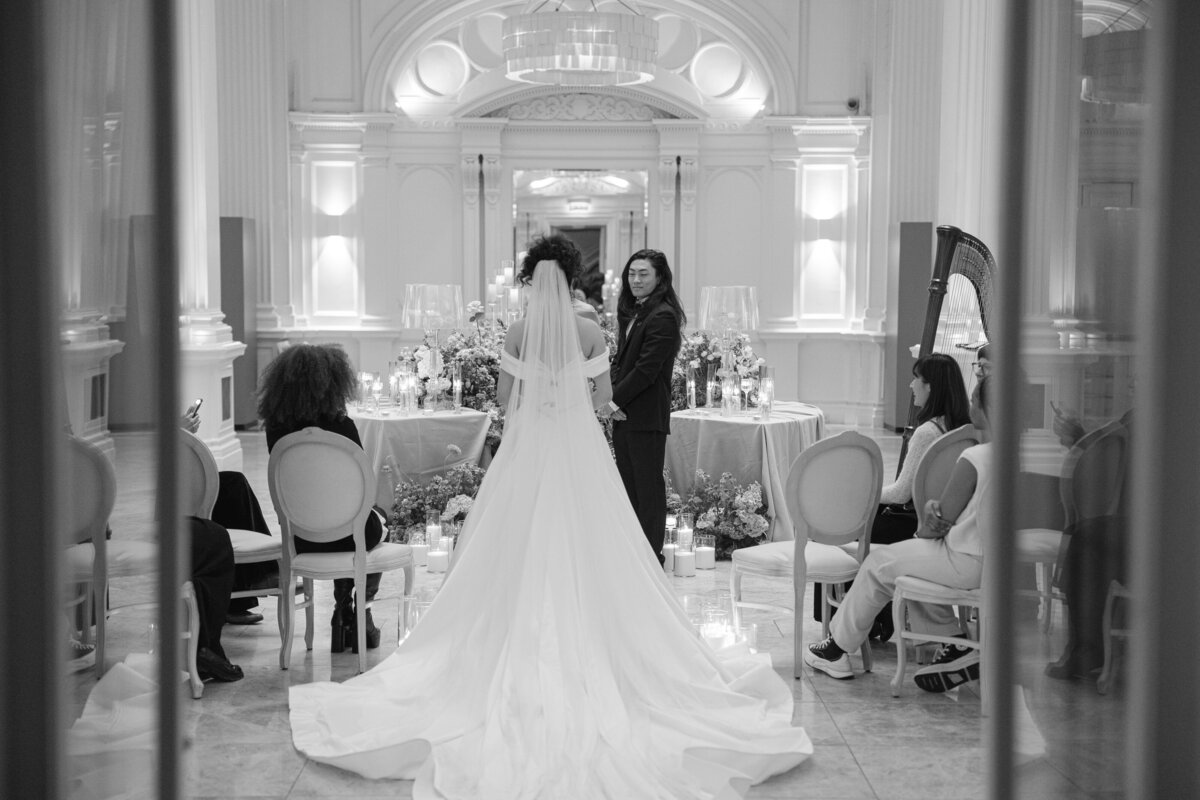 Black-and-white photo of a modern multicultural wedding ceremony at Andaz Hotel London, showing the bride walking down the aisle toward her partner, captured by Chi Ramos Photography