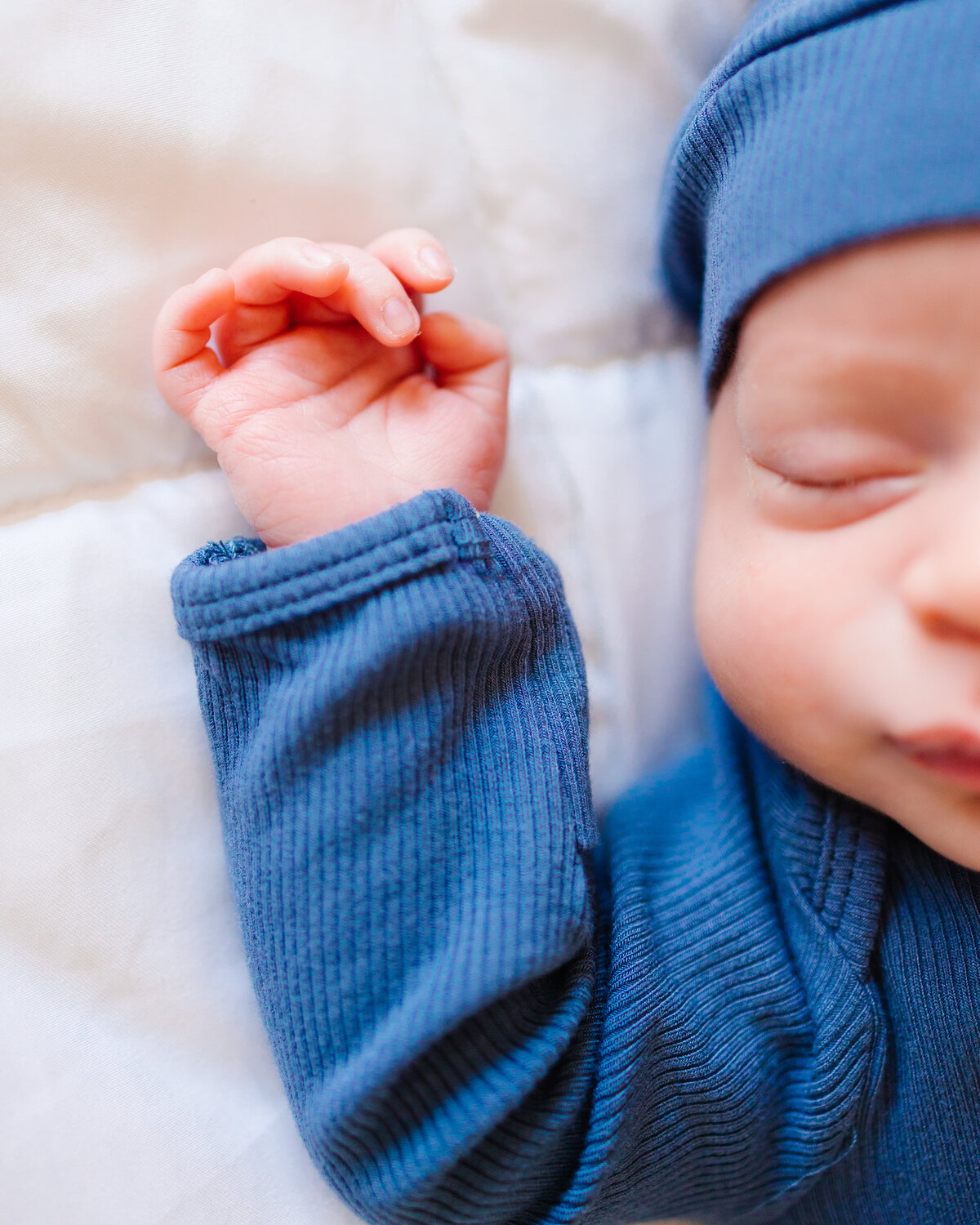 Photograph of the hand and face of a newborn baby dressed in a dark blue outfit