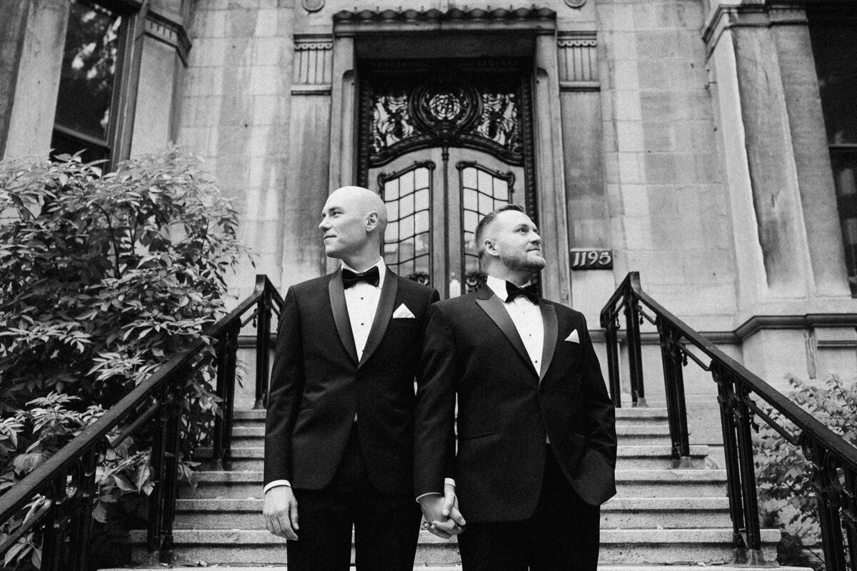 Deux mariés en tuxedos devant un immeuble de Montréal pendant leur journée de mariage.