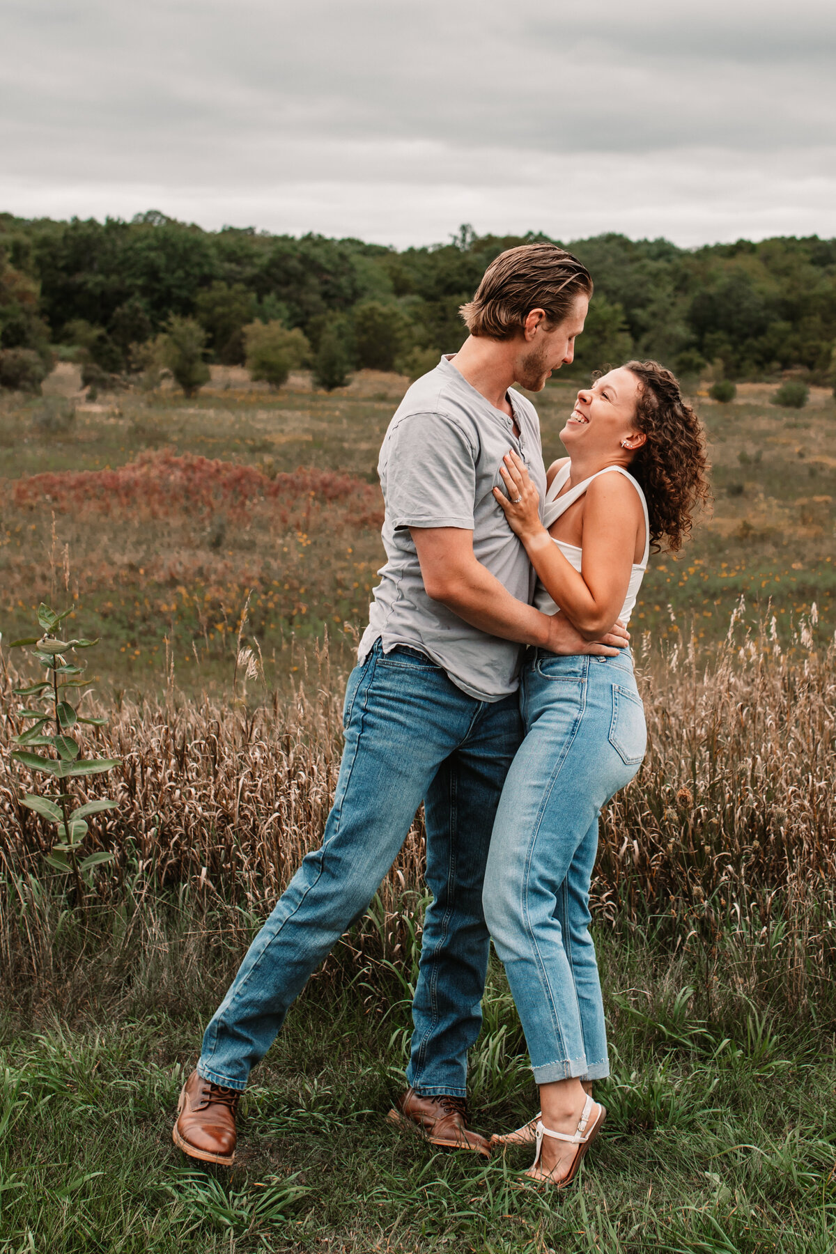 man and woman laugh together in a field wearing jeans